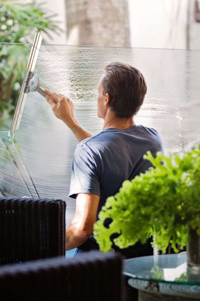 شركة تنظيف A man cleaning a glass barrier outdoors with a squeegee, surrounded by greenery.